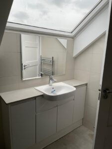 A straightforward washroom with white tiled walls, a toilet, and a hand washing area
